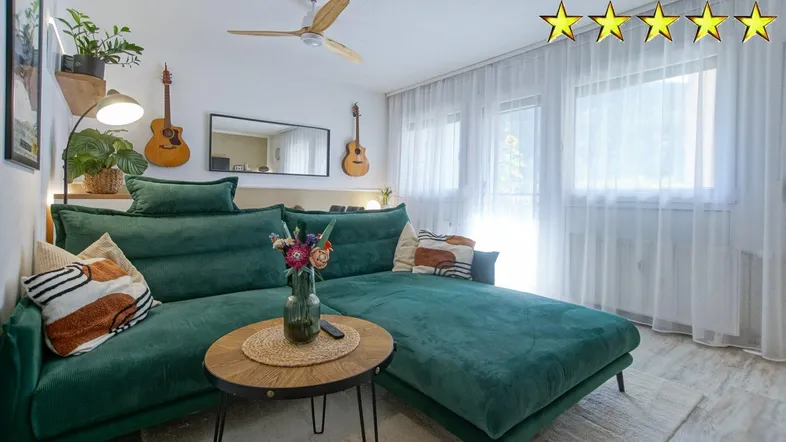 Helles Wohnzimmer mit bequemer grüner Couch, Deckenventilator und großen Fenstern für viel Tageslicht.