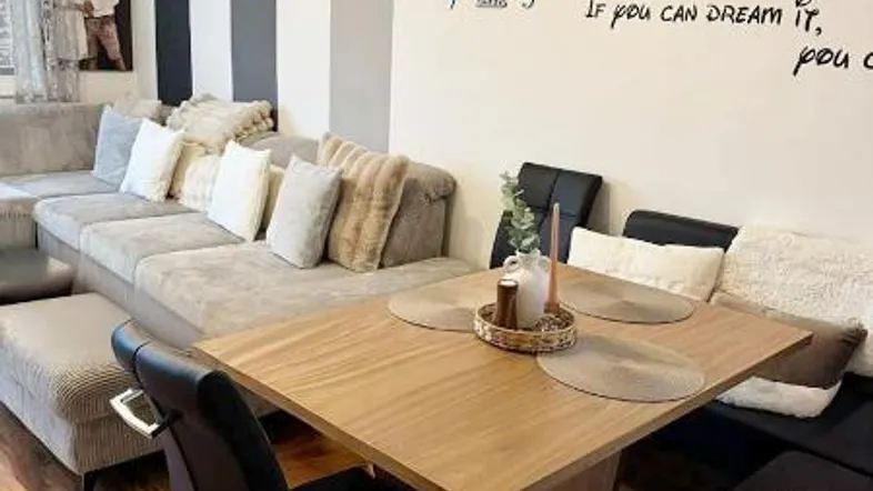 Gemütlicher Wohn- und Essbereich mit großem Sofa, Esstisch und moderner Wanddekoration.