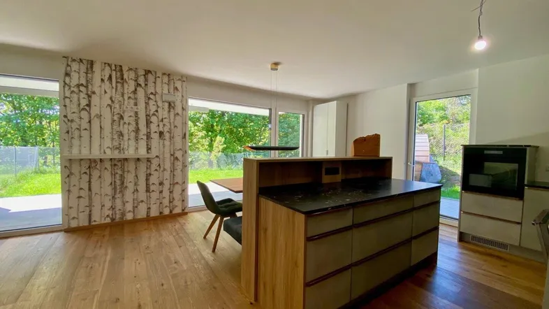 Funktionale Kücheninsel mit Arbeitsfläche und Blick ins Grüne durch die großen Fenster.