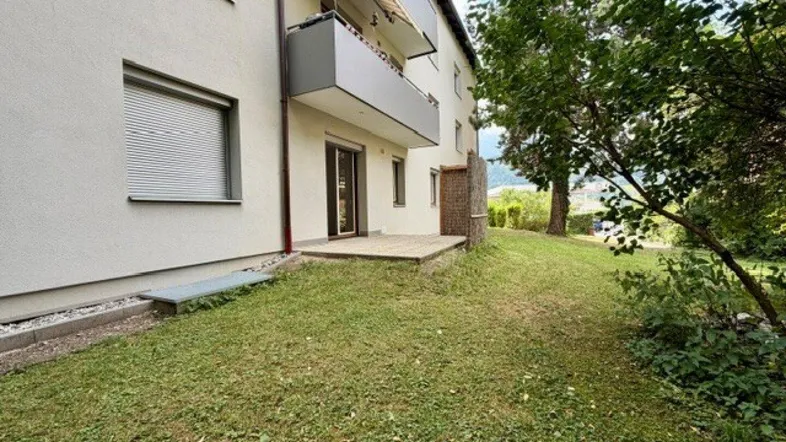 Außenansicht des Gebäudes mit einer kleinen Terrasse und einem Rasenbereich im Vordergrund.
