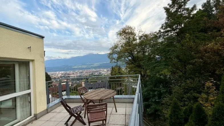 Geräumige Terrasse mit Sitzgelegenheiten und weitem Blick über die Stadt und die umliegenden Berge.