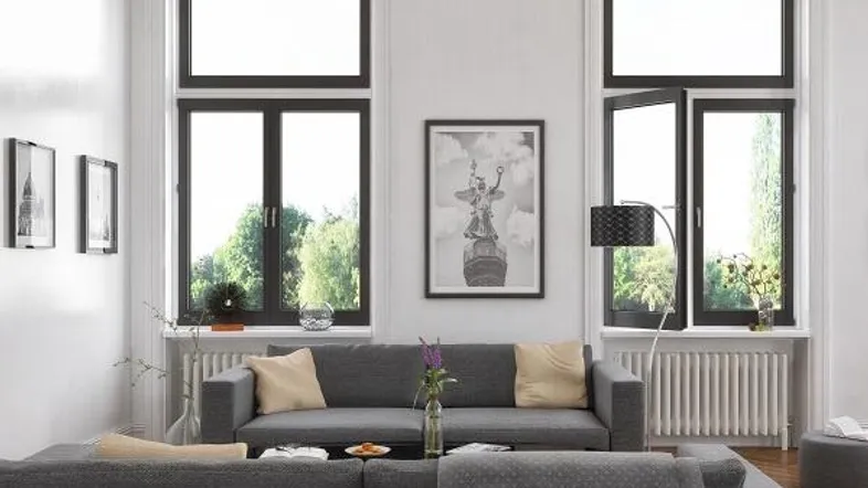 Helles Wohnzimmer mit modernem grauem Sofa, hohen Fenstern und Blick ins Grüne.