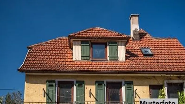 Gelbe Hausfassade mit rotem Ziegeldach, grünen Fensterläden und Dachgauben unter blauem Himmel.