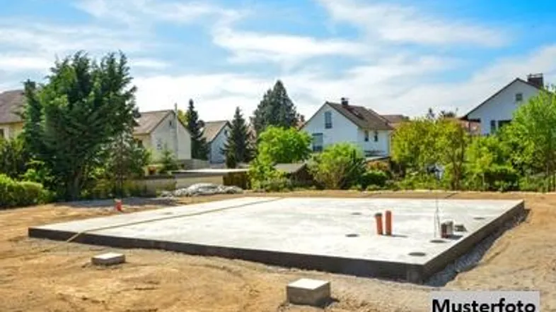 Betonfundament für ein neues Haus auf einem Baugrundstück mit umliegender Bebauung und viel Grün.
