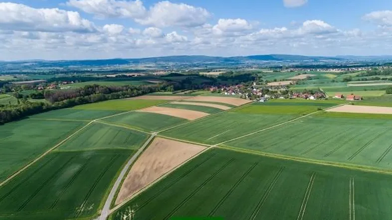 Luftaufnahme einer ländlichen Landschaft mit grünen Feldern und einem Dorf in der Ferne unter blauem Himmel.