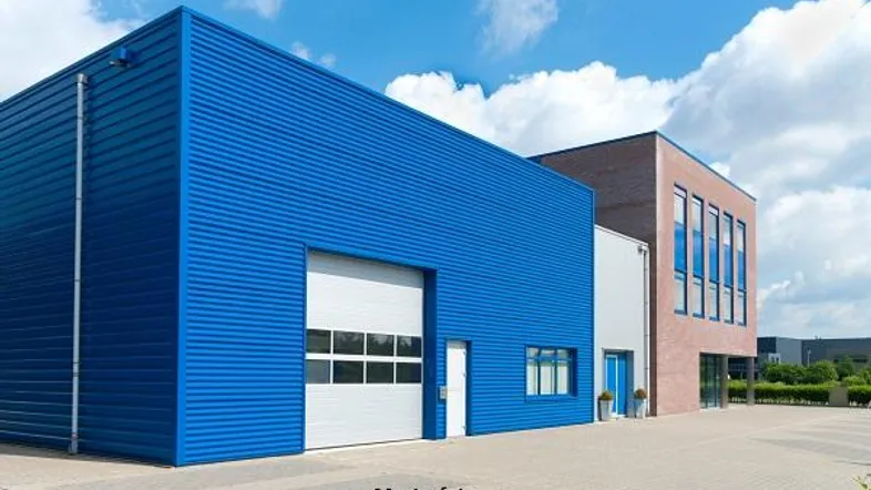 Modernes Industriegebäude mit blauer Fassade, großem Garagentor und angrenzendem Bürotrakt.