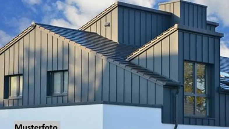 Moderne Hausfassade mit grauer Metallverkleidung und weißem Sockel unter blauem Himmel.