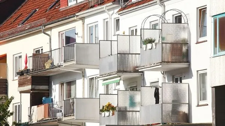 Mehrere Balkone an einer Wohnhausfassade mit roten Ziegeldächern und weißen Wänden, die auf einen sonnigen Tag hindeuten.