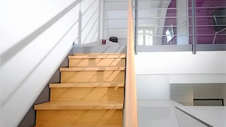 Heller Innenbereich mit moderner Holztreppe und Galerie, die zu einem oberen Bereich führt.