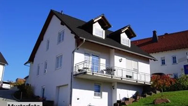 Weißes Einfamilienhaus mit dunklem Satteldach, Gauben und einem Balkon in ländlicher Umgebung.