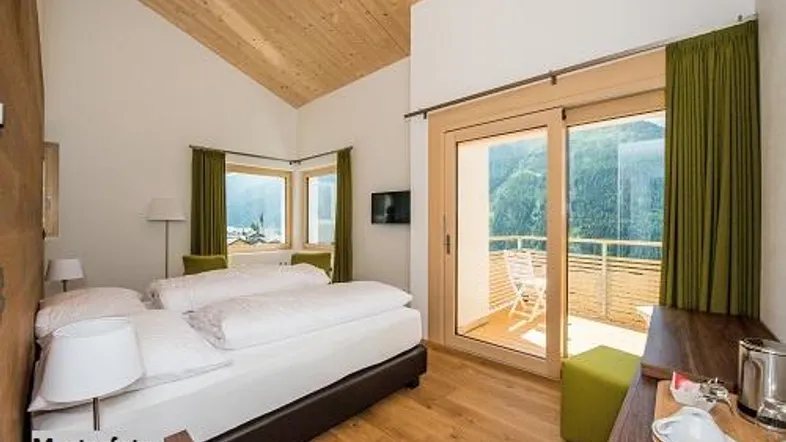 Helles Schlafzimmer mit Holzbalkendecke, Zugang zum Balkon und Bergblick, ausgestattet mit modernen Möbeln.