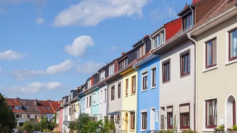 Reihenhäuser mit bunten Fassaden und Satteldächern entlang einer Wohnstraße unter blauem Himmel.
