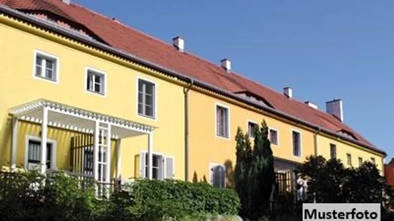 Gelbes Gebäude mit rotem Ziegeldach, grüner Bepflanzung und einem kleinen Vordach.