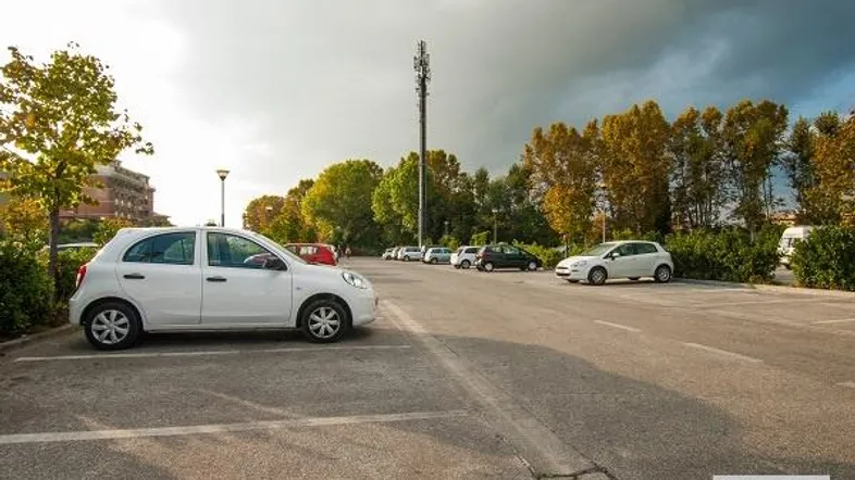 Ein Parkplatz mit mehreren Autos und Bäumen unter einem bewölkten Himmel.