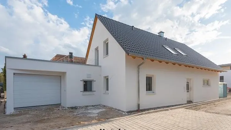 Neubau-Einfamilienhaus mit weißer Fassade, Satteldach und integrierter Garage unter blauem Himmel.