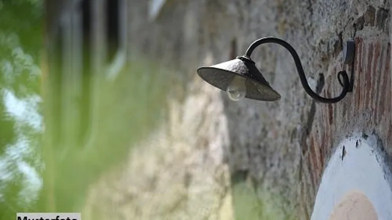 Alte schmiedeeiserne Außenlampe an einer rustikalen Steinmauer, die das Gebäude beleuchtet.