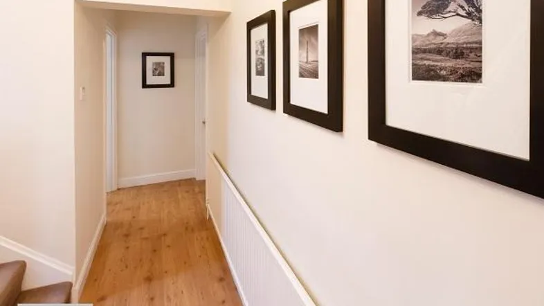 Heller Flur mit Holzfußboden und gerahmten Bildern an der Wand, der zu weiteren Räumen führt.