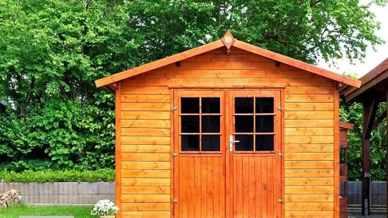 Ein charmantes Holzgartenhaus mit Doppeltüren und Fenstern, umgeben von üppigem Grün im Garten.