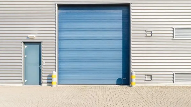 Fassade eines modernen Industriegebäudes mit großem blauen Rolltor und separatem Eingangsbereich.
