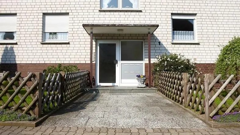Eingangsbereich eines Mehrfamilienhauses mit Rampe, Rollläden und gepflegter kleiner Grünfläche.
