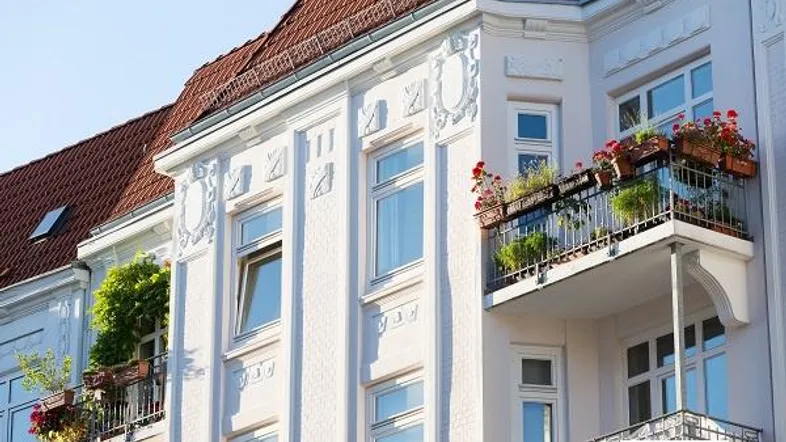 Historische Fassade eines Altbaus mit verzierten Balkonen und Blumenkästen unter blauem Himmel.