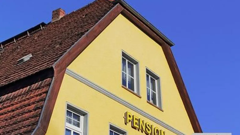 Gelbe Fassade eines älteren Gebäudes mit traditionellem Ziegeldach unter blauem Himmel.