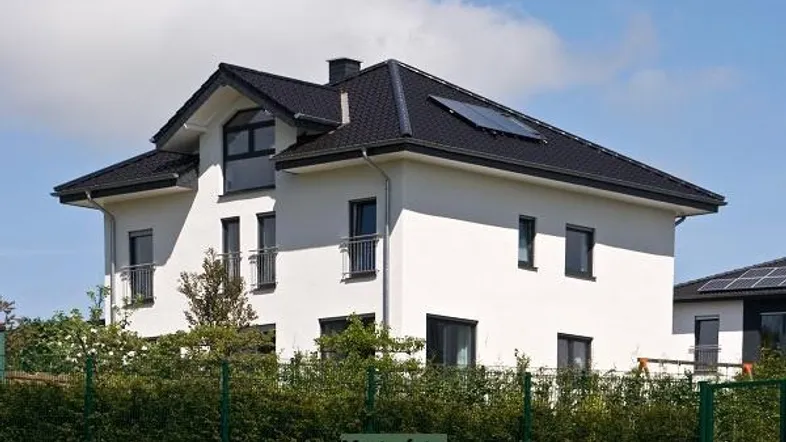 Modernes Einfamilienhaus mit weißer Fassade, schwarzem Satteldach und Solarpaneelen auf dem Dach.