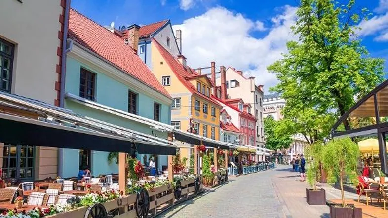 Belebte Straße mit farbenfrohen Gebäuden, Außencafés und blauem Himmel in einer historischen Stadt.