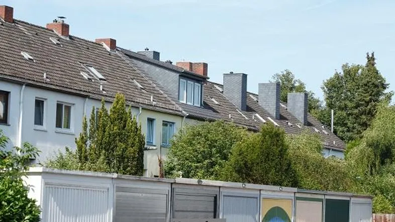 Reihenhäuser mit Satteldächern, Dachgauben und Schornsteinen, umgeben von Bäumen und Garagen im Vordergrund.