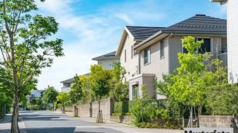 Reihenhäuser an einer ruhigen Straße mit viel Grün und blauem Himmel an einem sonnigen Tag.