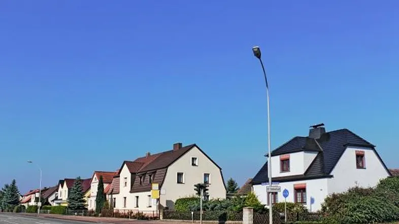 Reihen von Einfamilienhäusern entlang einer Straße unter blauem Himmel mit gepflegten Gärten.