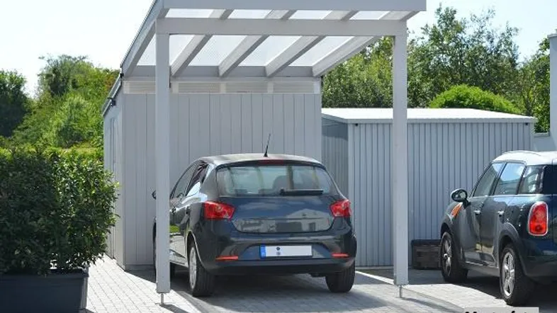 Heller Carport mit transparentem Dach und gepflastertem Stellplatz für ein Fahrzeug.