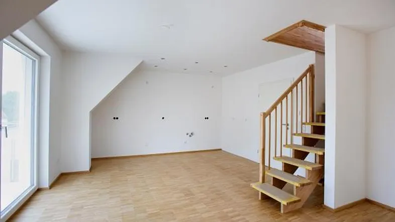 Heller Wohnraum mit Holzparkett, großen Fenstern und einer Holztreppe, die in eine obere Etage führt.