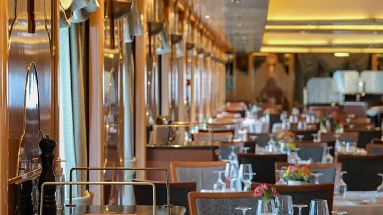 Elegantes Restaurant oder Speisesaal mit vielen gedeckten Tischen und warmem Licht, gekennzeichnet als Musterfoto.