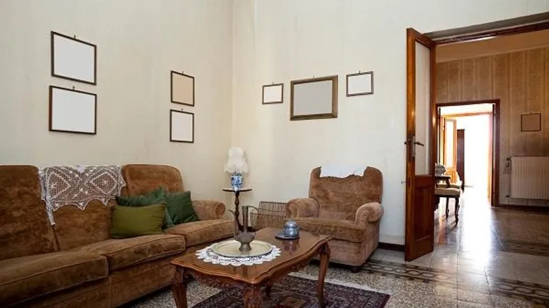 Traditionelles Wohnzimmer mit braunen Möbeln, gemusterten Fliesen und Blick in den Flur.