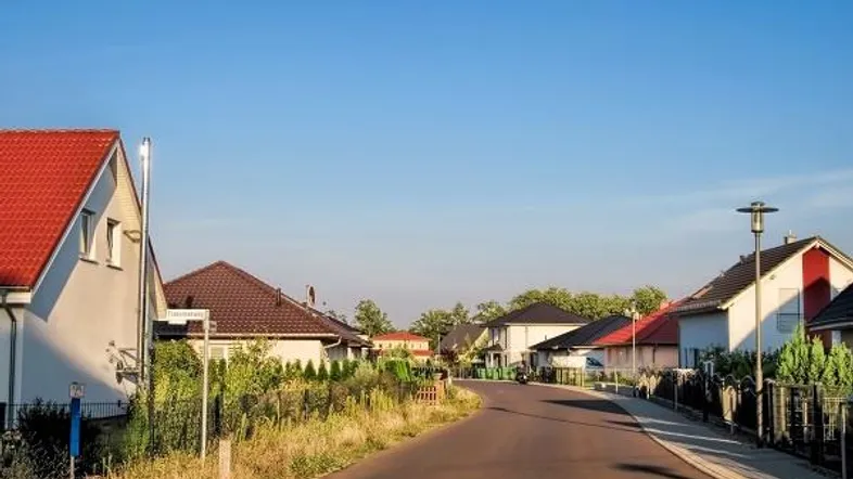 Wohnstraße mit Einfamilienhäusern und Gärten unter klarem blauem Himmel an einem sonnigen Tag.