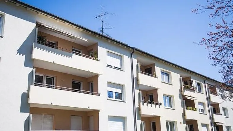 Mehrfamilienhaus mit mehreren Balkonen und Rollläden unter blauem Himmel an einem sonnigen Tag.