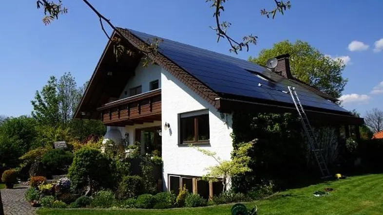 Freistehendes Haus mit Photovoltaikanlage auf dem Dach und gepflegtem Garten unter blauem Himmel.