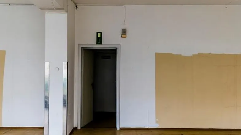 Leerer Innenraum mit hohen Decken, teilweise gestrichenen Wänden und Aufzugzugang.