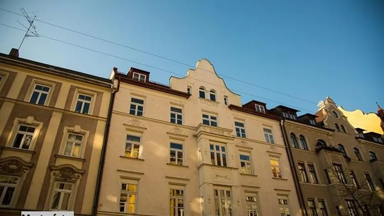 Historische Fassade eines Mehrfamilienhauses mit vielen Fenstern und dekorativen Giebeln unter blauem Himmel.