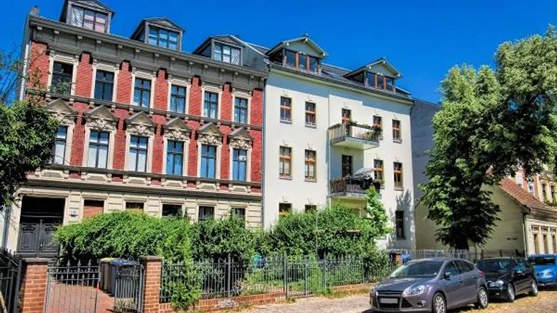 Historische Gebäude mit klassischer Architektur, gepflegter Fassade und Balkon an einem sonnigen Tag.