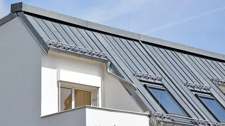 Modernes Gebäude mit grauem Metalldach, Dachfenstern und weißer Fassade.