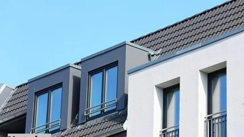 Moderne Dachgauben und weiße Fassade eines Neubaus unter blauem Himmel.
