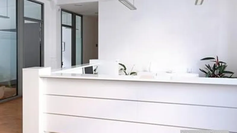 Moderner Empfangsbereich mit weißer Theke, großen Fenstern und Holzboden in einem Bürogebäude.