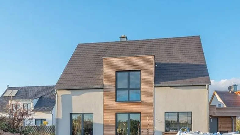 Modernes Einfamilienhaus mit Holzfassadenelementen und Satteldach unter blauem Himmel.