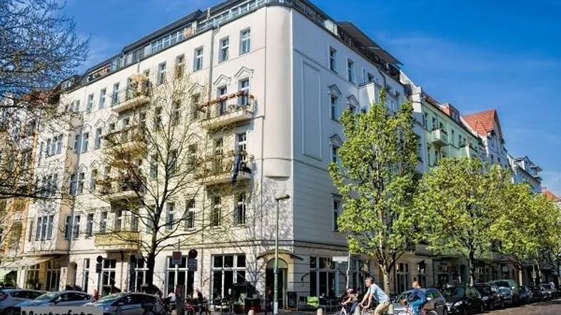 Mehrstöckiges Wohngebäude mit klassischer Fassade, Balkonen und Geschäften im Erdgeschoss an einer belebten Straße.