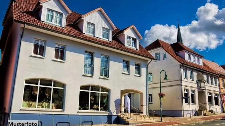 Historisches Gebäude mit weißer Fassade, rotem Satteldach und Gaubenfenstern an einer Straße.