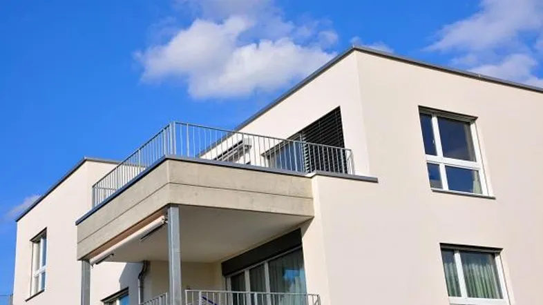 Moderne Fassade eines Mehrfamilienhauses mit Balkonen und großen Fenstern unter blauem Himmel.