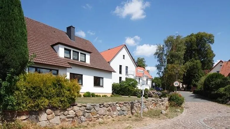Reihenhäuser mit Satteldächern und gepflegten Vorgärten an einer gepflasterten Straße unter blauem Himmel.