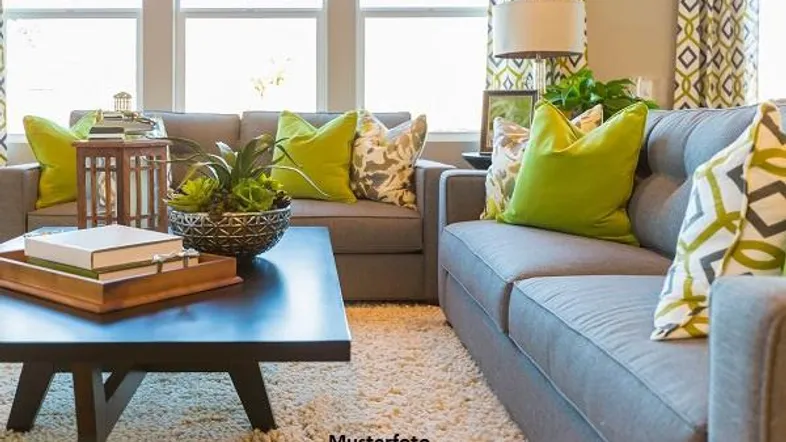 Helles Wohnzimmer mit grauen Sofas, grünen Kissen, einem Couchtisch und großen Fenstern.